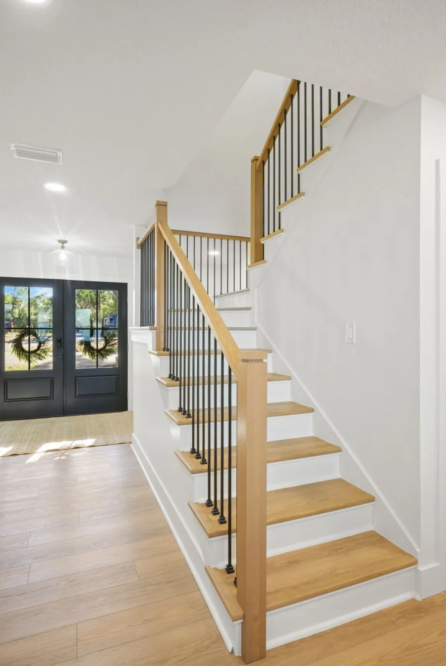 Entry staircase after renovation with white oak treads, white risers, square newel posts and black iron balusters