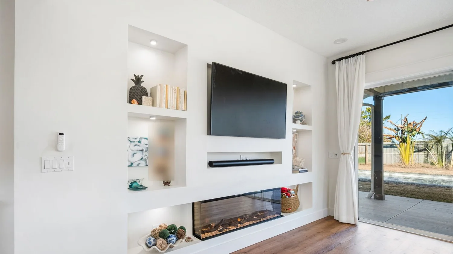 Living room after remodel with a built-in linear electric fireplace, lit display niches and a recessed soundbar shelf