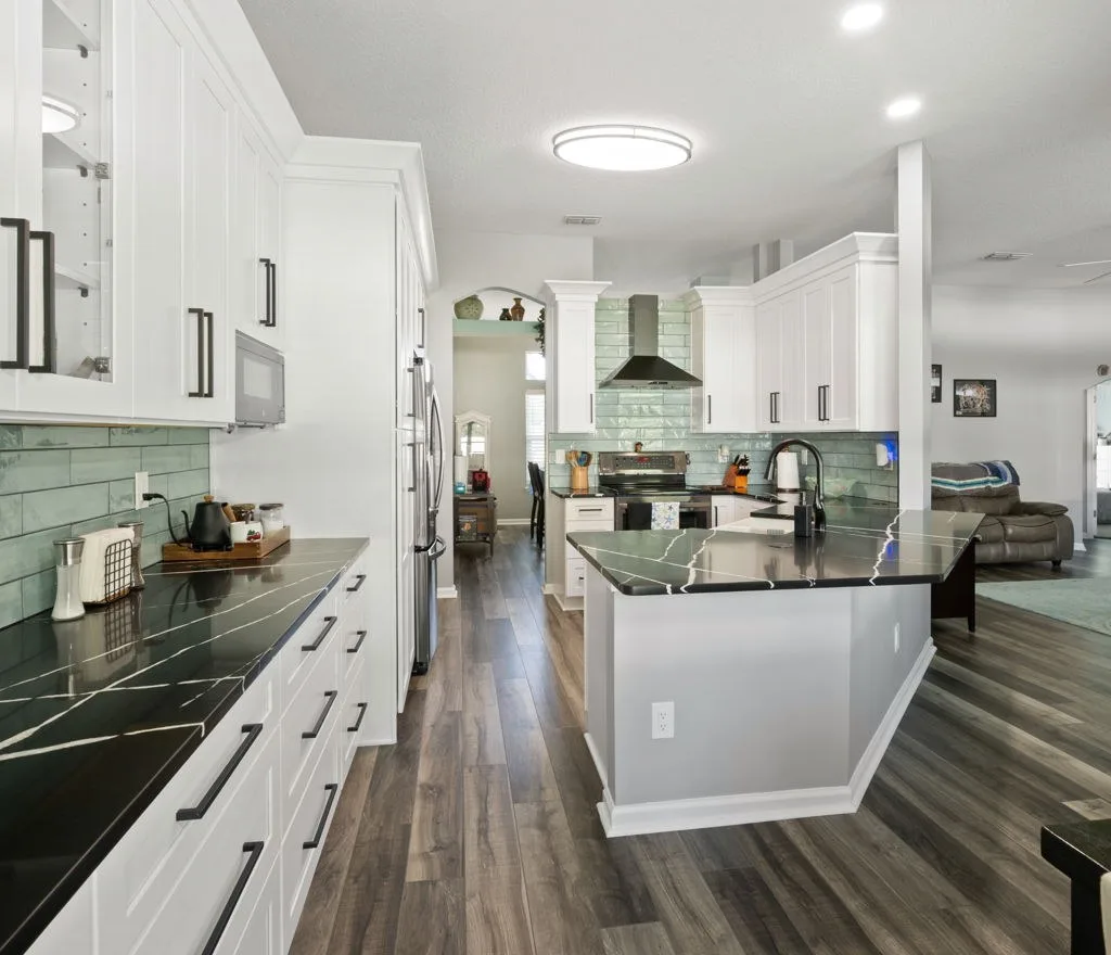 Kitchen after remodel with wide-plank wood-look flooring, white cabinetry and black quartz counters