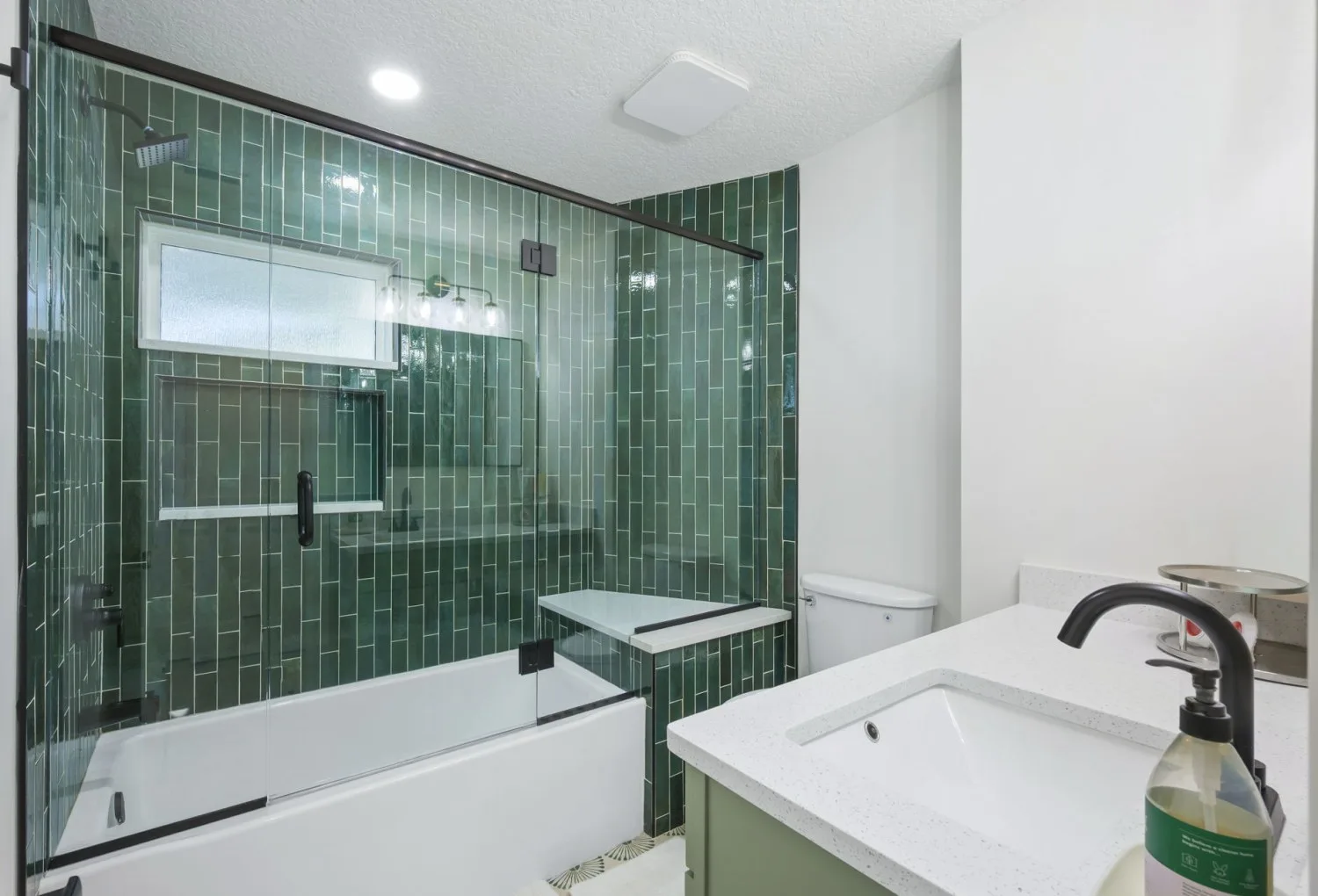 After: green vertical tile, frameless glass, built-in bench and quartz vanity