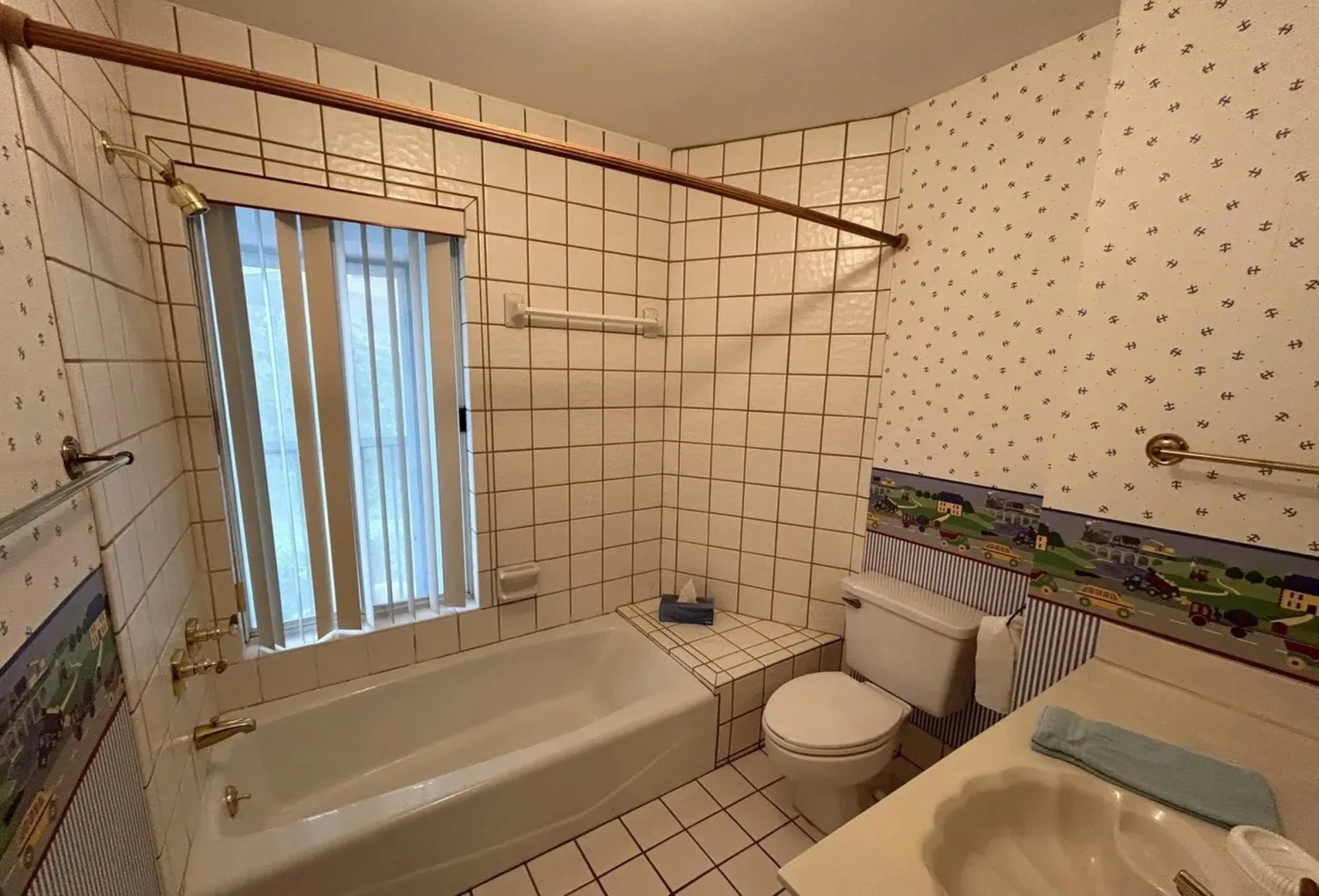 Before: guest bathroom with square tile, wallpaper border and brass fixtures