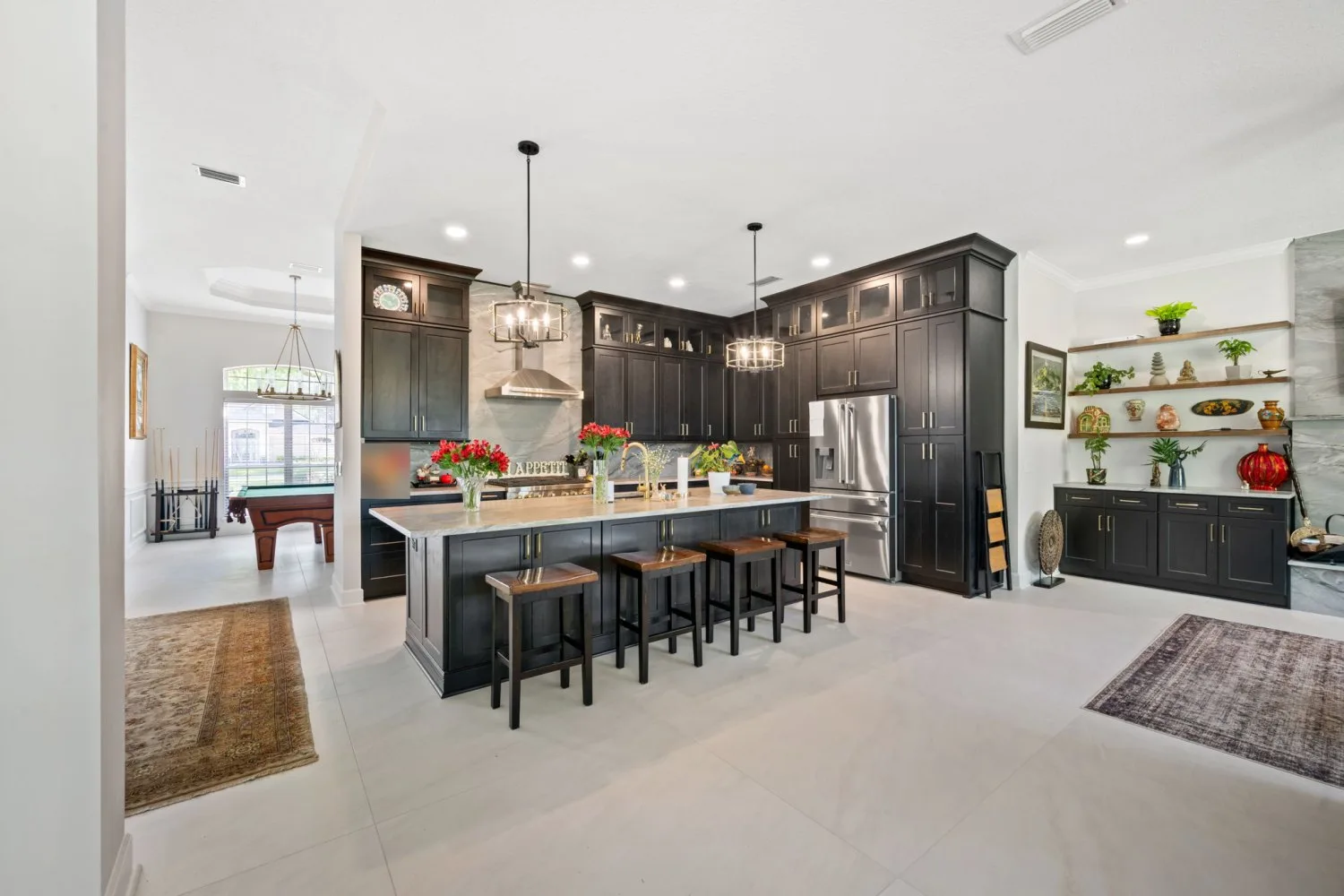 Open concept kitchen after remodel with dark shaker cabinetry, a long quartzite island and large-format tile