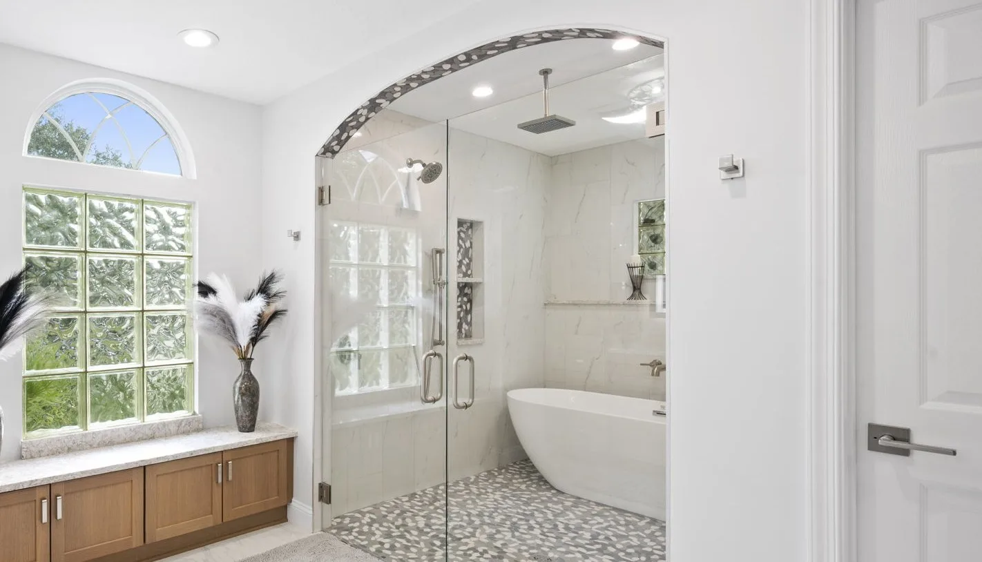 Primary bathroom after remodel with a tiled arch into a wet room with a freestanding tub, rain shower and pebble floor