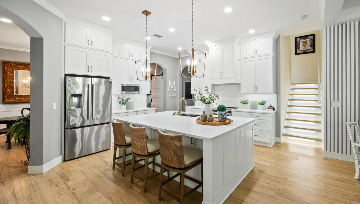 Kitchen after remodel with white shaker cabinetry, a large quartz island and brass lantern pendants